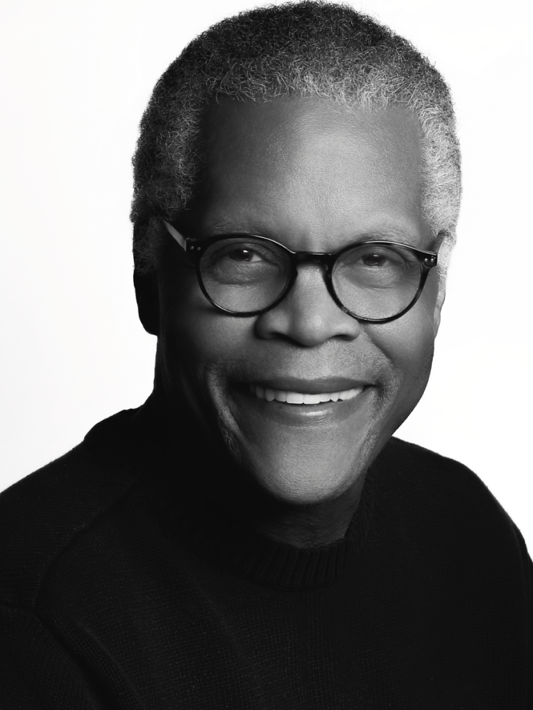 The image is a black-and-white headshot of the artist, smiling